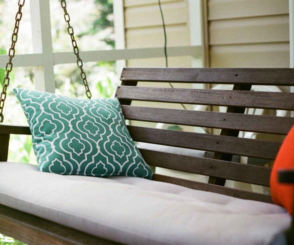 wooden porch swing with teal and red cushions